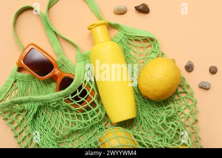 Bouteille de crème solaire, lunettes de soleil et sac à ficelle avec des citrons sur fond orange Banque D'Images