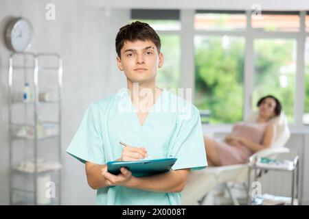 Jeune homme médecin posant dans le cabinet du médecin avec le document en main Banque D'Images