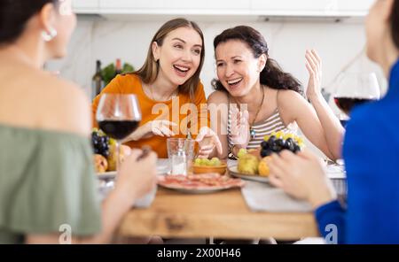 Des femmes heureuses se sont rassemblées autour d’une table festive, participant à des discussions animées et profitant des délices du vin Banque D'Images