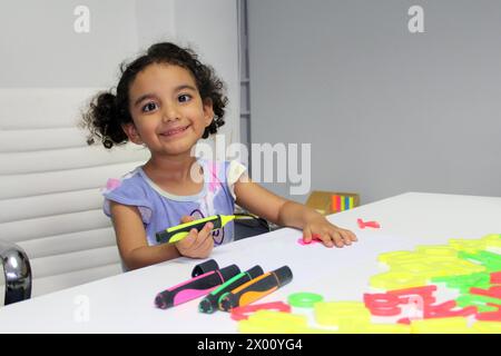 Fille brune Latina de 3 ans avec les cheveux bouclés dessine comme thérapie pour l'autisme et le trouble d'hyperactivité déficit de l'attention TDAH Banque D'Images