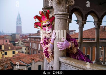 Une personne masquée féminine dans un costume créatif, posant sur l'escalier de la Scala Contarini del Bovolo, célébrant le Carnaval vénitien. Banque D'Images