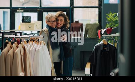 Femme senior et sa fille prennent des photos dans le grand magasin, profitant d'une journée de congé pour les achats de vêtements. Les clients souriants s'amusent avec des selfies dans un showroom de mode, une activité commerciale. Caméra A. Banque D'Images