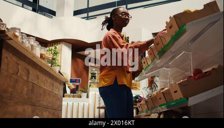 Client régulier mettant des légumes bio cultivés dans un sac en papier, allant faire des courses dans un magasin écologique zéro déchet. Femme soutenant les petites entreprises et un mode de vie durable. Caméra 2. Prise de vue sur trépied. Banque D'Images