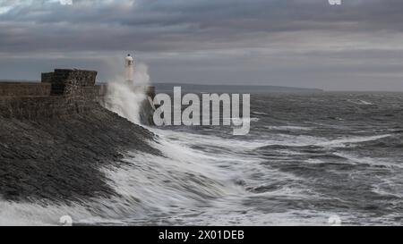 Mer agitée et vagues s'écrasant dans un mur de mer et un phare (Porthcawl, pays de Galles du Sud, Royaume-Uni) par un jour nuageux d'hiver Banque D'Images