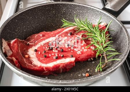 Un morceau de steak de bœuf grésille dans une poêle sur le poêle, un délicieux produit animal qui fait partie de nombreuses cuisines dans le monde entier Banque D'Images