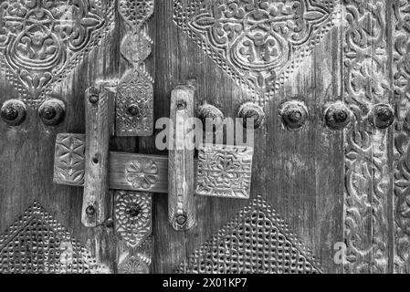 Image monochrome filtrée montrant les détails d'une serrure traditionnelle en bois sculptée à l'entrée d'une maison arabe traditionnelle restaurée. Banque D'Images