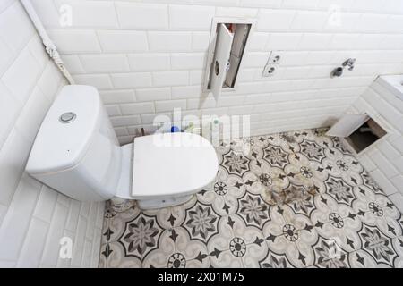 Intérieur des toilettes étroites avec toilettes murales avec murs blancs et sol en damier Banque D'Images