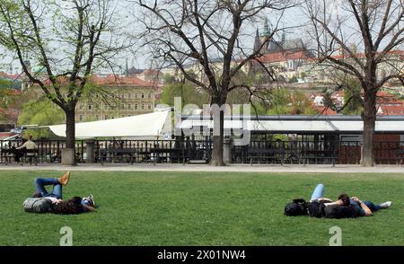 Les touristes se reposent dans un parc devant le château de Prague près de la rivière Vltava, au quai Alsovo à Prague, République tchèque, le 8 avril 2024. (CTK photo/Milos Ruml) Banque D'Images