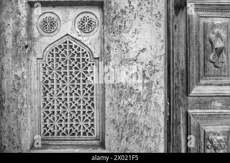 Monochrome, image filtrée d'un treillis de ventilation en plâtre à côté d'une porte boisée sculptée dans le mur extérieur en adobe d'un HO arabe traditionnel Banque D'Images