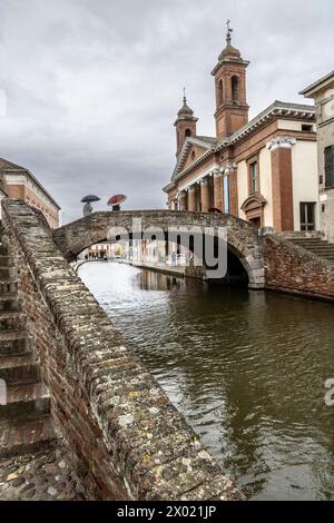 Comacchio, Ferrare, Italie : 03 avril 2024 : deux personnes avec parapluie devant la cathédrale San Cassiano à Comacchio dans la province de Ferrare Banque D'Images