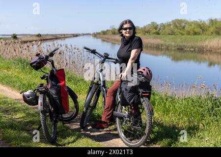 Femme roule sur un vélo électrique à travers le delta du Pô dans le nord de l'Italie Banque D'Images