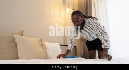 Homme afro-américain faisant le ménage à la maison le week-end, lit de nettoyage et chambre de nettoyage Banque D'Images