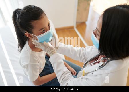 Fille malade en masque médial regardant le médecin palpant ses ganglions lymphatiques du cou Banque D'Images