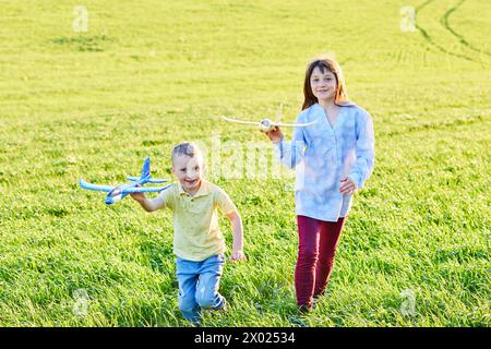 Garçon et fille courant tenant deux avions jaune et bleu jouet dans le champ pendant la journée ensoleillée d'été Banque D'Images