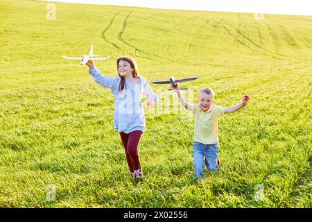 Garçon et fille courant tenant deux avions jaune et bleu jouet dans le champ pendant la journée ensoleillée d'été Banque D'Images