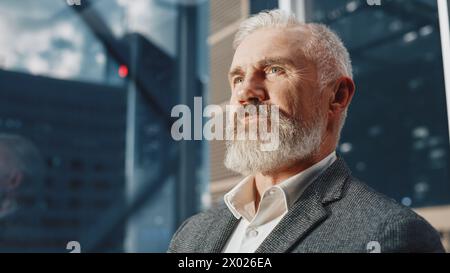 Portrait d'un homme d'affaires d'âge moyen réussi dans un ascenseur en verre de cheval de costume au bureau dans le centre d'affaires moderne. Homme regardant les gratte-ciel modernes du centre-ville par la fenêtre Panorama dans l'ascenseur. Banque D'Images