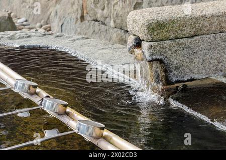 Un mur de pierre avec une fontaine de pierre au milieu. La fontaine est entourée d'une grille métallique Banque D'Images