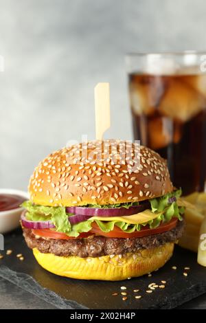 Hamburger avec délicieuse patty, boisson gazeuse, frites et sauce sur table sur fond gris, gros plan Banque D'Images