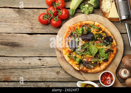 Délicieuse pizza végétarienne et ingrédients sur table en bois, plat. Espace pour le texte Banque D'Images