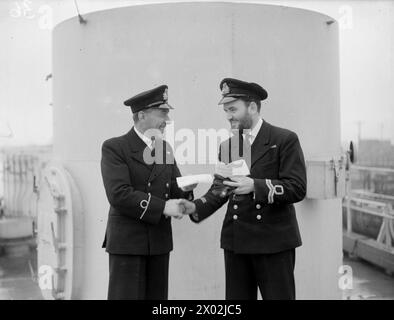 LES FRÉGATES D'ESCORTE OBTIENNENT DEUX U-BOOTS DE PLUS. 30 MARS 1944, BELFAST. LES FRÉGATES DU 1ER GROUPE D'ESCORTE, LE HMS AFFLECK, ET SES NAVIRES JUMEAUX GORE, GOULD ET GARLIES DÉTRUISENT DEUX SOUS-MARINS DANS L'ATLANTIQUE. PHOTOS DE RETOUR DU GROUPE. - Pères fiers du voyage, avec des télégrammes leur racontant des événements heureux à la maison, se félicitant les uns les autres. De gauche à droite : M. l B Phipps (artilleur) de Plymouth, qui a un fils, serrant la main à Surg Lieut A K Mighton, RNVR, de Hamilton (Ontario), qui a une fille. Ils servent tous deux à bord du HMS AFFLECK Banque D'Images