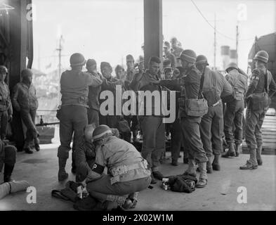 LIBÉRATION DE L'EUROPE : CAPTURÉE EN FRANCE. 18 JUIN 1944, PLYMOUTH. LES PRISONNIERS DE GUERRE ALLEMANDS PRIS DANS LA TÊTE DE PONT ARRIVENT À UN PORT BRITANNIQUE EN ROUTE POUR LES CAMPS DE PRISONNIERS DE GUERRE. - Les soldats américains fouillent les prisonniers allemands quand ils arrivent à terre Banque D'Images