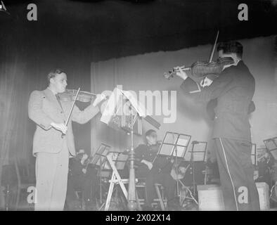 MENUHIN JOUE POUR LA FLOTTE BRITANNIQUE. SEPTEMBRE 1944, SCAPA FLOW. LORS DE L'UN DES CONCERTS DONNÉS PAR YEHUDI MENUHIN, VIOLONISTE DE RENOMMÉE MONDIALE, À LA FLOTTE BRITANNIQUE. IL A ÉTÉ DIVERTI DANS LE NAVIRE AMIRAL PAR LE C IN C, L'AMIRAL SIR HENRY MOORE, KCB, CVO, DSO. - Menuhin, accompagné d'un orchestre de Royal Marines, jouant le second violon d'un violoniste marin Banque D'Images