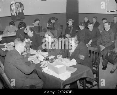 EAST HAM INFORMATION BUREAU : WAR WELFARE WORK IN LONDON, 1941 - trois femmes, dont une membre du Women's Voluntary Service (WVS), s'adressent à des agents d'information du département de relogement et de mise en forme du Bureau d'information d'East Ham. Ils demandent tous de nouvelles maisons, car les leurs ont été gravement damées ou détruites par des raids aériens. Derrière les femmes, deux rangées de personnes peuvent être vues, toutes attendant patiemment leur tour Banque D'Images