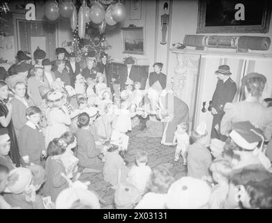 FÊTE DE NOËL DE L'AMIRAUTÉ POUR LES ENFANTS DES OFFICIERS DE MARINE ALLIÉS. MAISON DE L'AMIRAUTÉ, 17 DÉCEMBRE 1942, MME A. V ALEXANDER, ÉPOUSE DU PREMIER SEIGNEUR DE L'AMIRAUTÉ, A DIVERTI LES ENFANTS DES NATIONS ALLIÉES À UN THÉ DE NOËL À LA MAISON DE L'AMIRAUTÉ. PARMI LES INVITÉS PRÉSENTS SE TROUVAIENT MME WINSTON CHURCHILL, MME ERNEST BEVIN, MME MAISKY, MME DUNCAN SANDYS, MME LEE, MME RANDOLPH CHURCHILL, MME ATLEE, ET BIEN D'AUTRES PERSONNALITÉS BIEN CONNUES. - Père Noël a un cadeau pour Jennifer Evinson, petite-fille de Mr A V Alexander, à droite Mme Atlee portant l'uniforme de la Croix-Rouge. En arrière-plan se trouve Mme Alex Banque D'Images