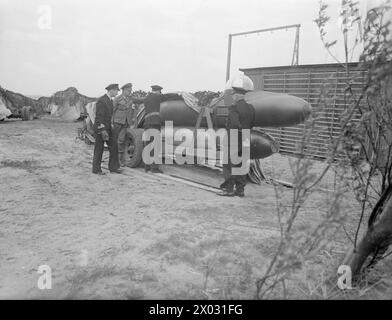 "TORPILLE HUMAINE" ALLEMANDE. MAI 1945, FORT LYNAES, DANEMARK. TORPILLES HUMAINES ALLEMANDES ET SOUS-MARINS NICHÉS PRÊTS À ÊTRE TRANSPORTÉS VERS LA MER. - Officier de marine britannique armé, avec des officiers danois et allemands, inspectant l'une des "torpilles humaines" allemandes. D'autres sont en arrière-plan couverts et camouflés Banque D'Images