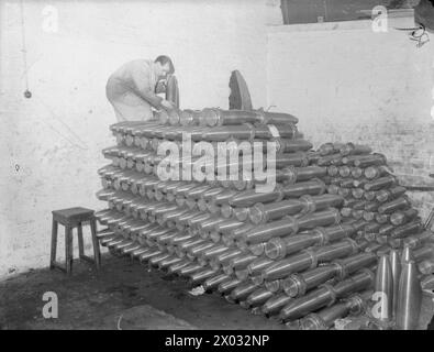 AU TRAVAIL DANS Une USINE BRITANNIQUE D'OBUS, ANGLETERRE, C 1940 - Un ouvrier de munitions ajoute à une pile de munitions lourdes finies dans une usine britannique d'obus Banque D'Images