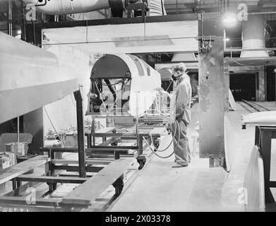 De Havilland Tiger Moth entraîne la production d'avions en Grande-Bretagne entre 1939 et 1945, montrant le fuselage sur des chaînes de montage en mouvement à travers une cabine de peinture avec un ouvrier d'usine portant un masque de protection. Banque D'Images
