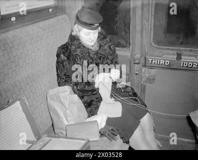 LES CARTER EN TEMPS DE GUERRE : LA VIE QUOTIDIENNE D'Une FAMILLE BRITANNIQUE SUR LE FRONT INTÉRIEUR, ANGLETERRE, C 1940 - Mme carter est assise dans un wagon de chemin de fer et tricote un vêtement pour l'un de ses deux enfants. Elle voyage de London Victoria à Hayward's Heath, Sussex, pour rendre visite à ses enfants, qui ont été évacués là-bas Banque D'Images