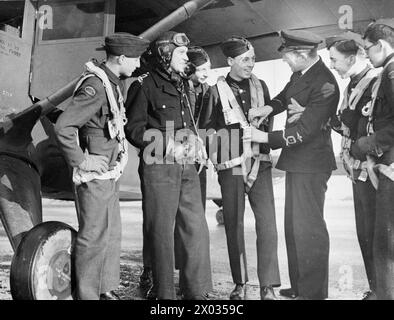 LES GARÇONS DE L'ATC VISITENT LA STATION AÉRIENNE DE LA MARINE ROYALE À BURSCOUGH, POTERIES. 9 FÉVRIER 1945, LORS DE LA VISITE D'UN GROUPE DE GARÇONS ATC À LA BASE AÉRIENNE DE LA ROYAL NAVY. LA VISITE FAISAIT PARTIE DE LEUR FORMATION. - Un officier de Fleet Air Arm explique l'installation du harnais de parachute aux cadets de l'ATC pendant que le pilote regarde Banque D'Images