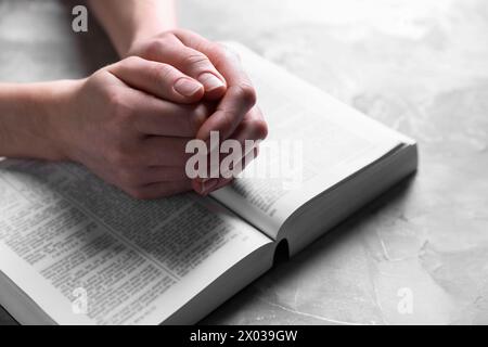 Religion. Femme chrétienne priant sur la Bible à la table texturée grise, gros plan Banque D'Images