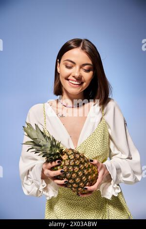 Une jeune femme aux cheveux bruns tient joyeusement un ananas frais dans un cadre de studio lumineux. Banque D'Images