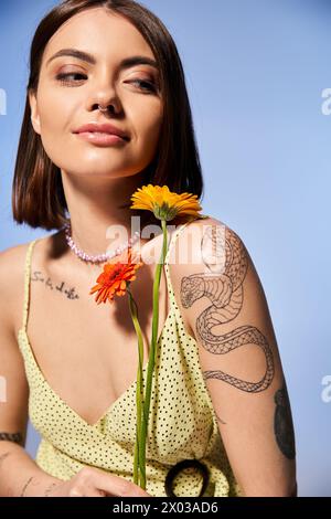 Une jeune femme aux cheveux bruns vêtue d'une robe jaune, tenant délicatement une fleur vibrante. Banque D'Images