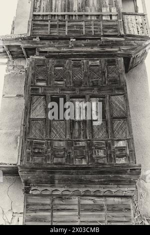 Une vue filtrée monochrome d'un balcon en bois sculpté en décomposition à l'extérieur d'une maison abandonnée dans la ville saoudienne de Yanbu. Banque D'Images