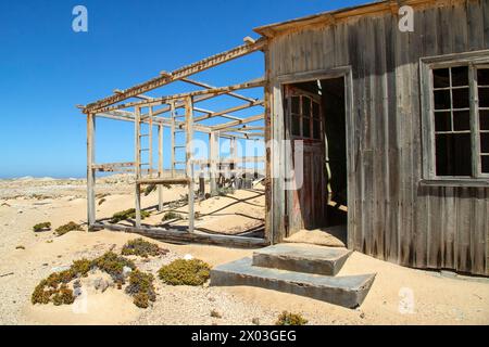 Le penchant et autrefois la porte rouge d'une maison de mineur abandonnée, préservée par l'air sec du désert, à la mine Borgenfels dans la zone interdite en Namibie. Banque D'Images