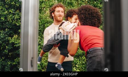 Loving Mixed Race Family jouant avec un adorable bébé garçon à Modern Home, suspendu dans le jardin. Mère joyeuse nourrissant un enfant. Concept d'enfance, Nouvelle vie, parentalité. Banque D'Images