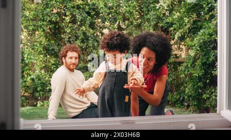 Loving Mixed Race Family jouant avec un adorable bébé garçon à Modern Home, suspendu dans le jardin. Mère joyeuse nourrissant un enfant. Concept d'enfance, Nouvelle vie, parentalité. Banque D'Images