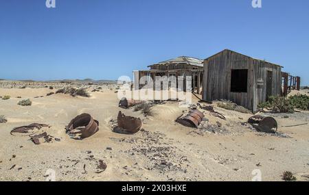 Abandonnée, maison de mineur de bois avec des barils de pétrole pold dans le sable au premier plan, préservée par l'air sec du désert, à la mine Borgenfels dans le Forbidde Banque D'Images