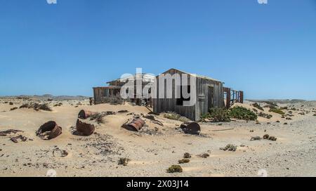 Abandonnée, maison de mineur de bois avec des barils de pétrole pold dans le sable au premier plan, préservée par l'air sec du désert, à la mine Borgenfels dans le Forbidde Banque D'Images