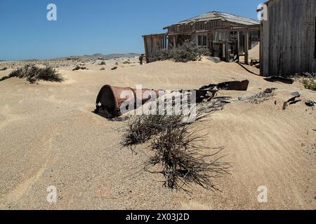 Abandonnée, maison de mineur de bois avec de vieux barils de pétrole dans le sable au premier plan, préservée par l'air sec du désert, à la mine Bogenfels dans le Spergebeit Banque D'Images