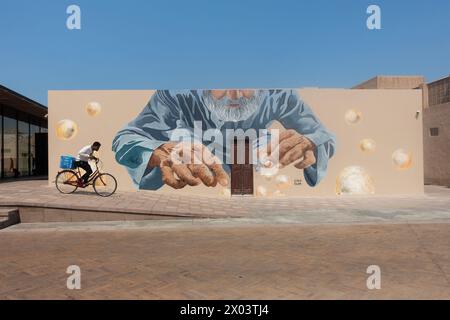 Cycliste passe devant une murale géante dans le quartier historique d'Al Shindagha, Dubaï, Émirats arabes Unis. Banque D'Images