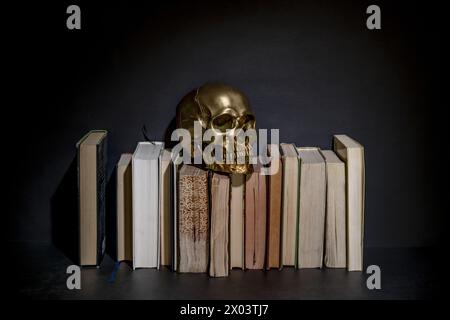 Une nature morte avec un crâne doré sur une pile de vieux livres Banque D'Images