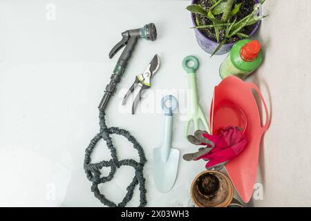 Nature morte avec arrosoir pour saumon, gants de protection, avec tuyau vert sur la terrasse d'un grenier avec des murs en béton et en métal ondulé Banque D'Images