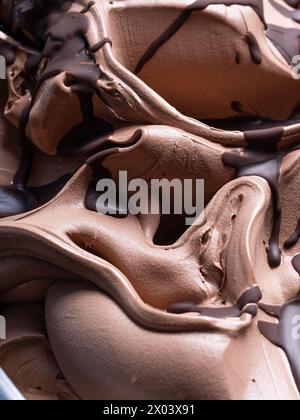 Gelato congelé à saveur de chocolat - détail plein cadre. Gros plan d'une texture de surface brune de crème glacée au chocolat recouverte d'une garniture de chocolat noir. Banque D'Images