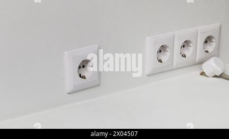 Quatre prises électriques sur un mur de lumière et une fiche électrique avec un fil. Fiche électrique blanche qui n'est pas branchée sur une prise électrique. Banque D'Images