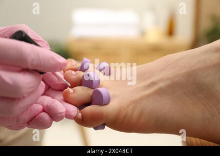 Pédicuriste professionnel peignant les ongles des orteils du client avec du vernis dans le salon de beauté, gros plan Banque D'Images