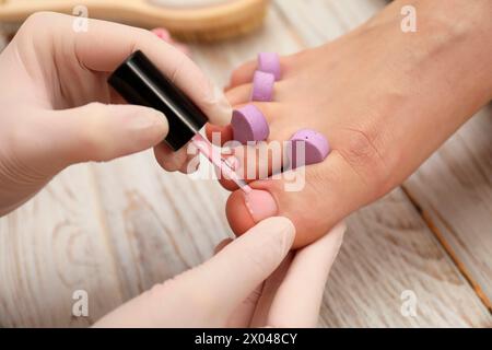 Pédicuriste professionnel peignant les ongles des orteils du client avec du vernis dans le salon de beauté, gros plan Banque D'Images